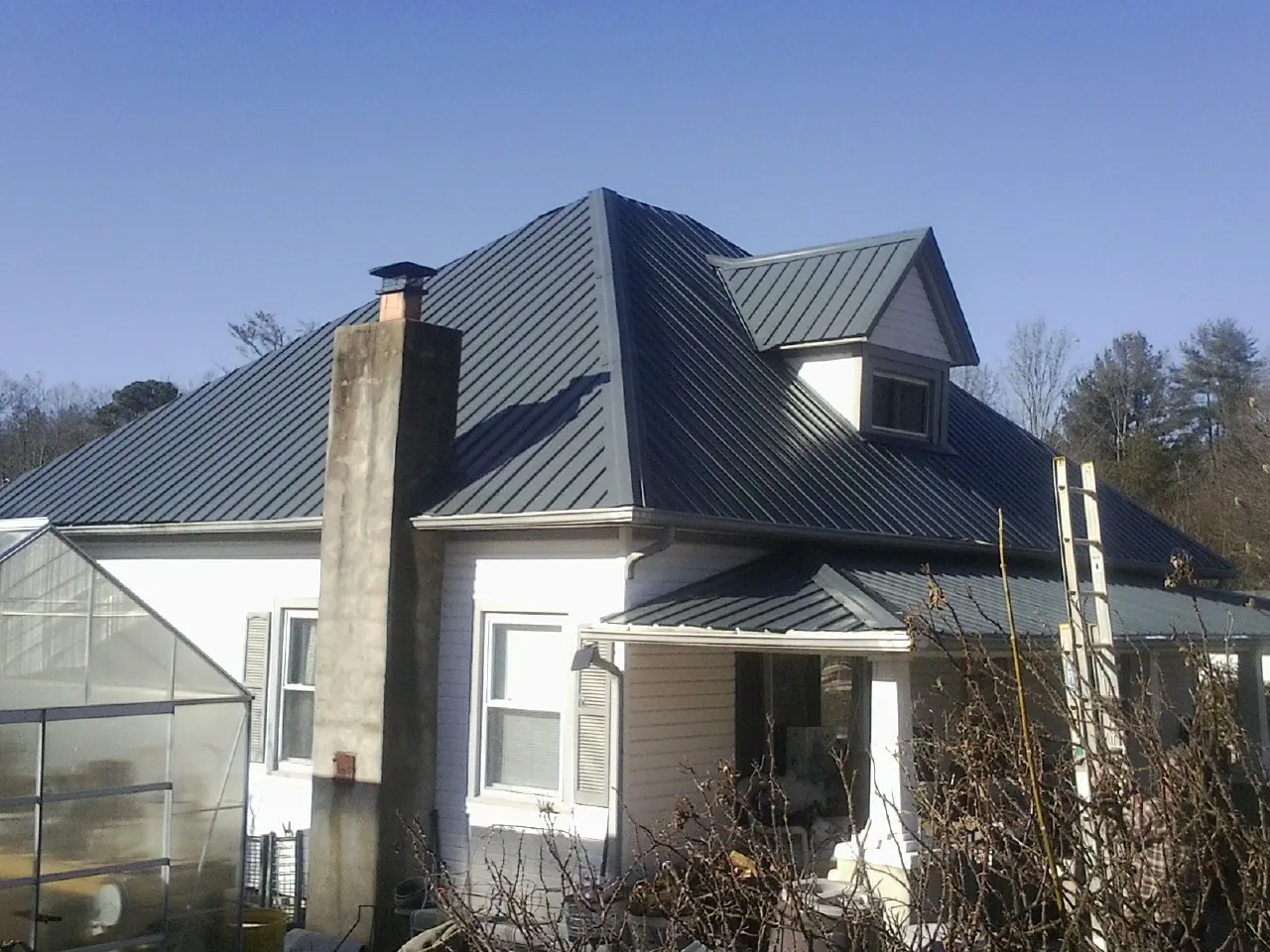 Dark blue standing seam metal roof on a white farmhouse with dormer — Slate & Tile Roof Repair by Roofing Brothers in Fort Atkinson