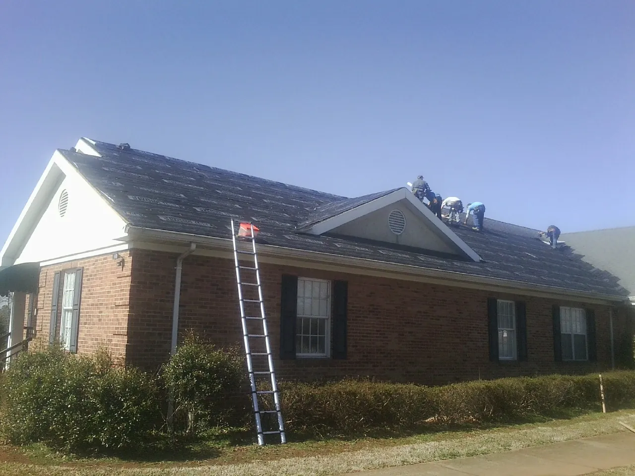 Crew tearing shingles off a brick ranch roof with a ladder set — Emergency Roof Repair work by our crew in Fort Atkinson