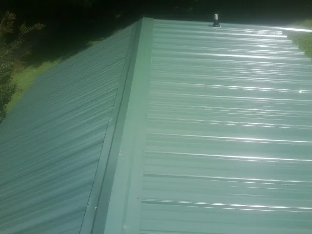 New green metal panels meeting at the ridge of a roof — Flat Roof Repair work by our crew in Fort Atkinson
